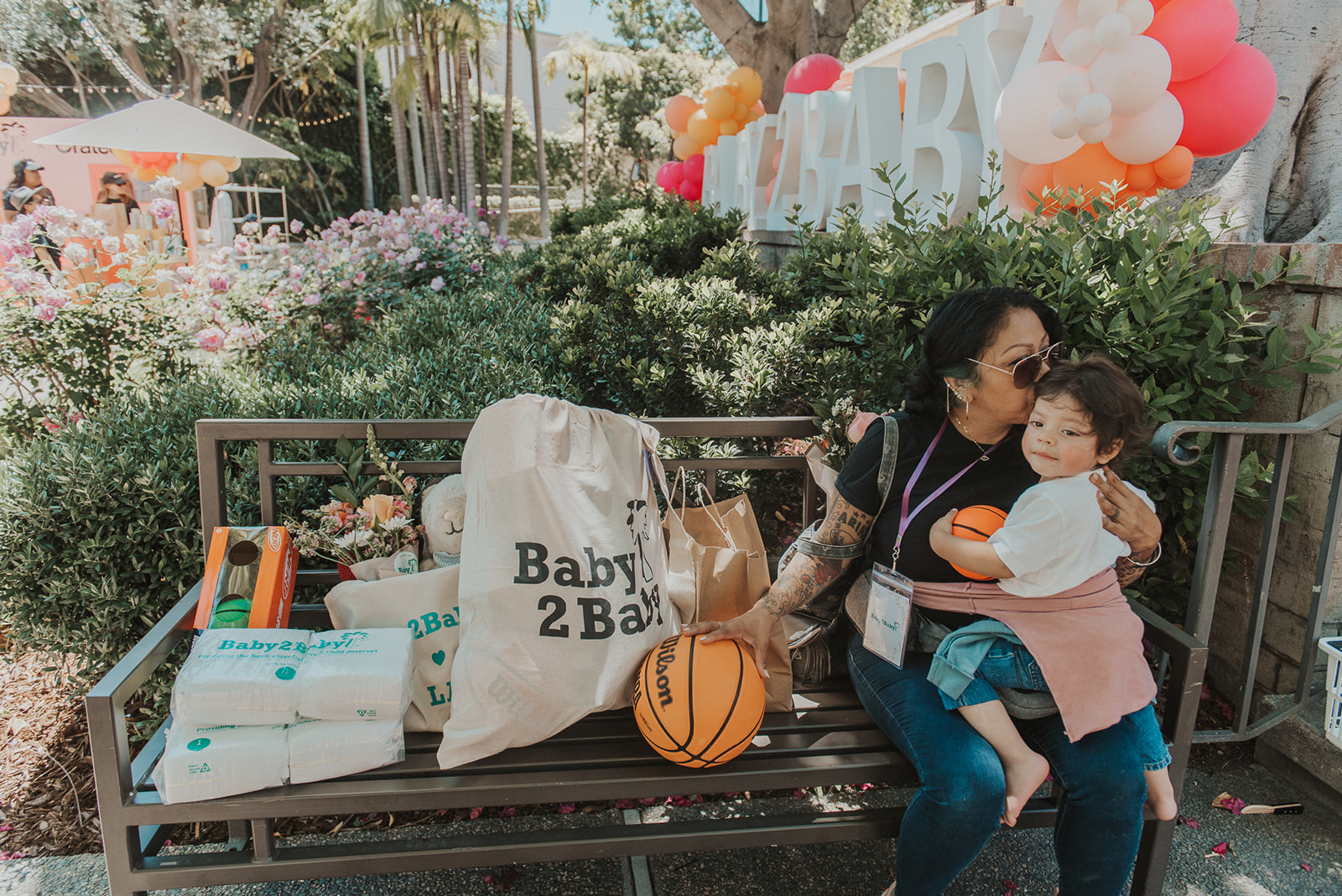 A mom kissing her baby on a bench surrounded by toys and baby supplies