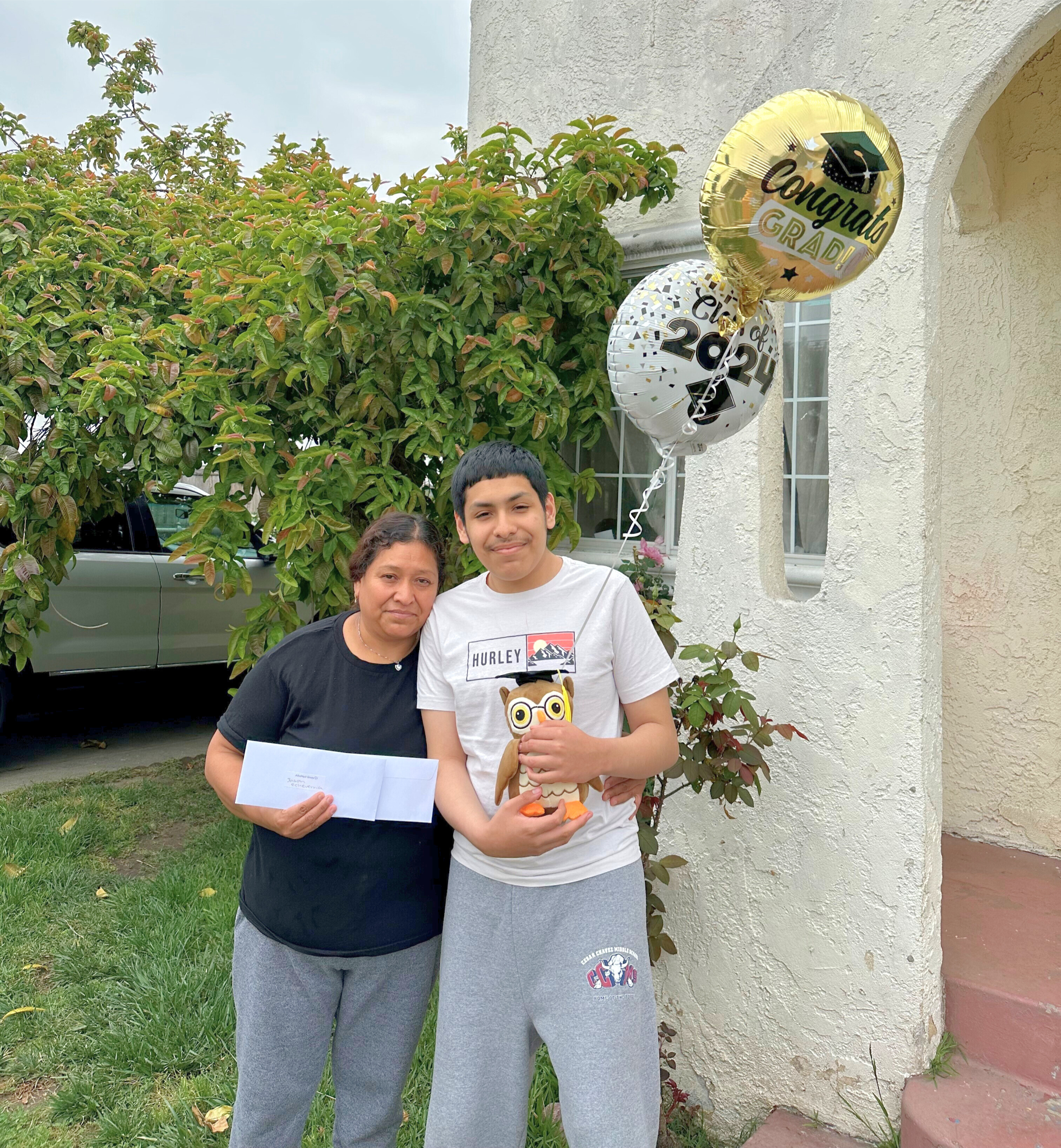 A teenage boy and his mom standing with graduation balloons and gift cards.