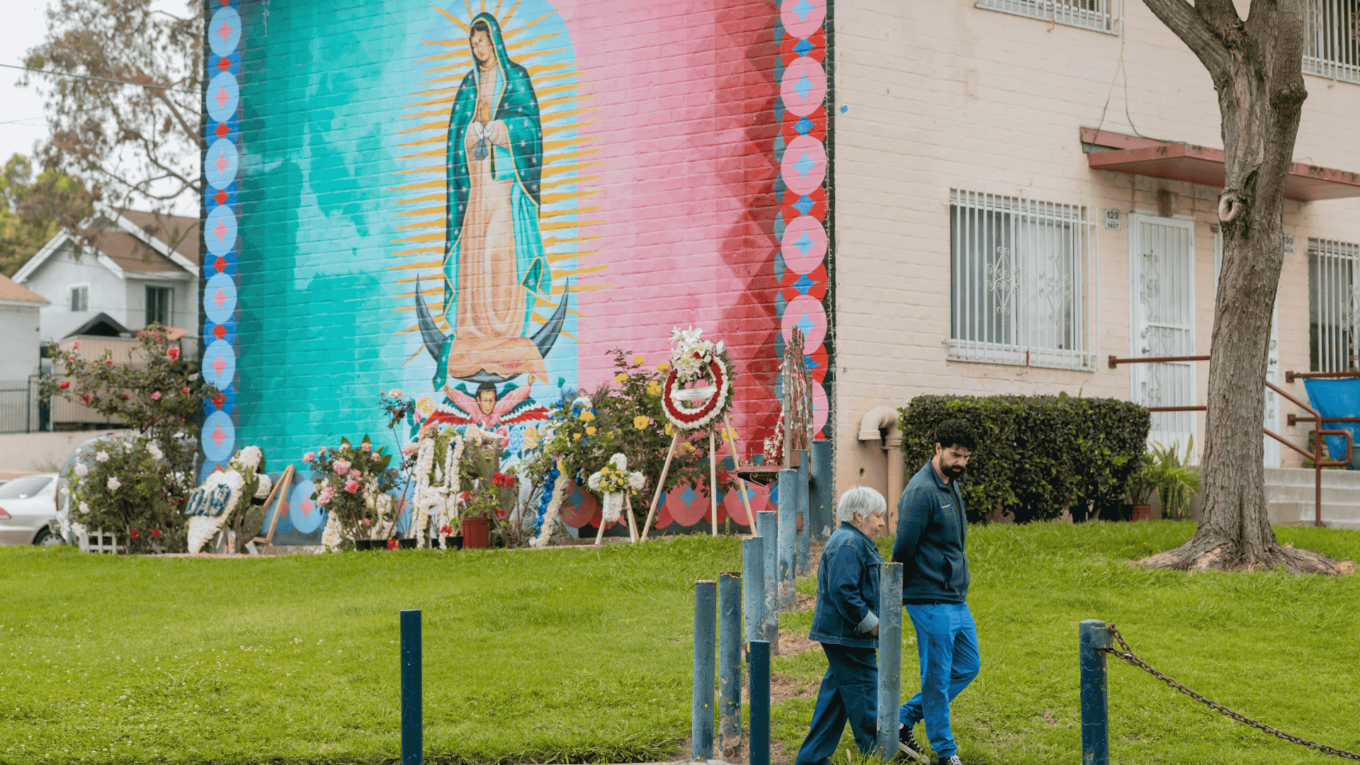 A doctor and a senior patient walking in front of a mural of the Virgin Mary
