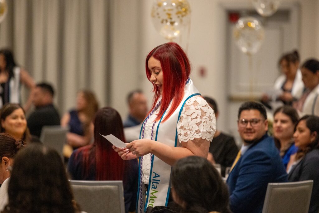 Nursing graduate looking down at a sheet of paper, reciting the Nightingale Nursing Pledge.
