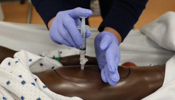 Close up of student's hands performing a needle insertion on the training manikin.