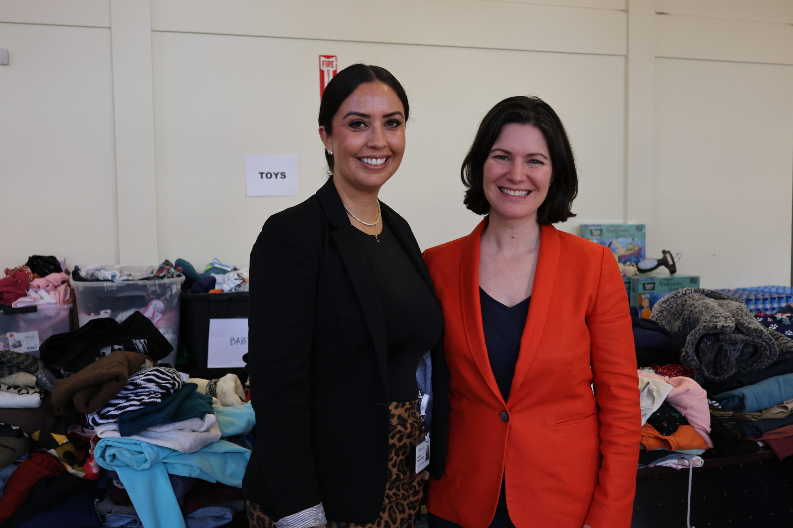 Two leaders dressed in professional attire stand in front of emergency aid supplies.